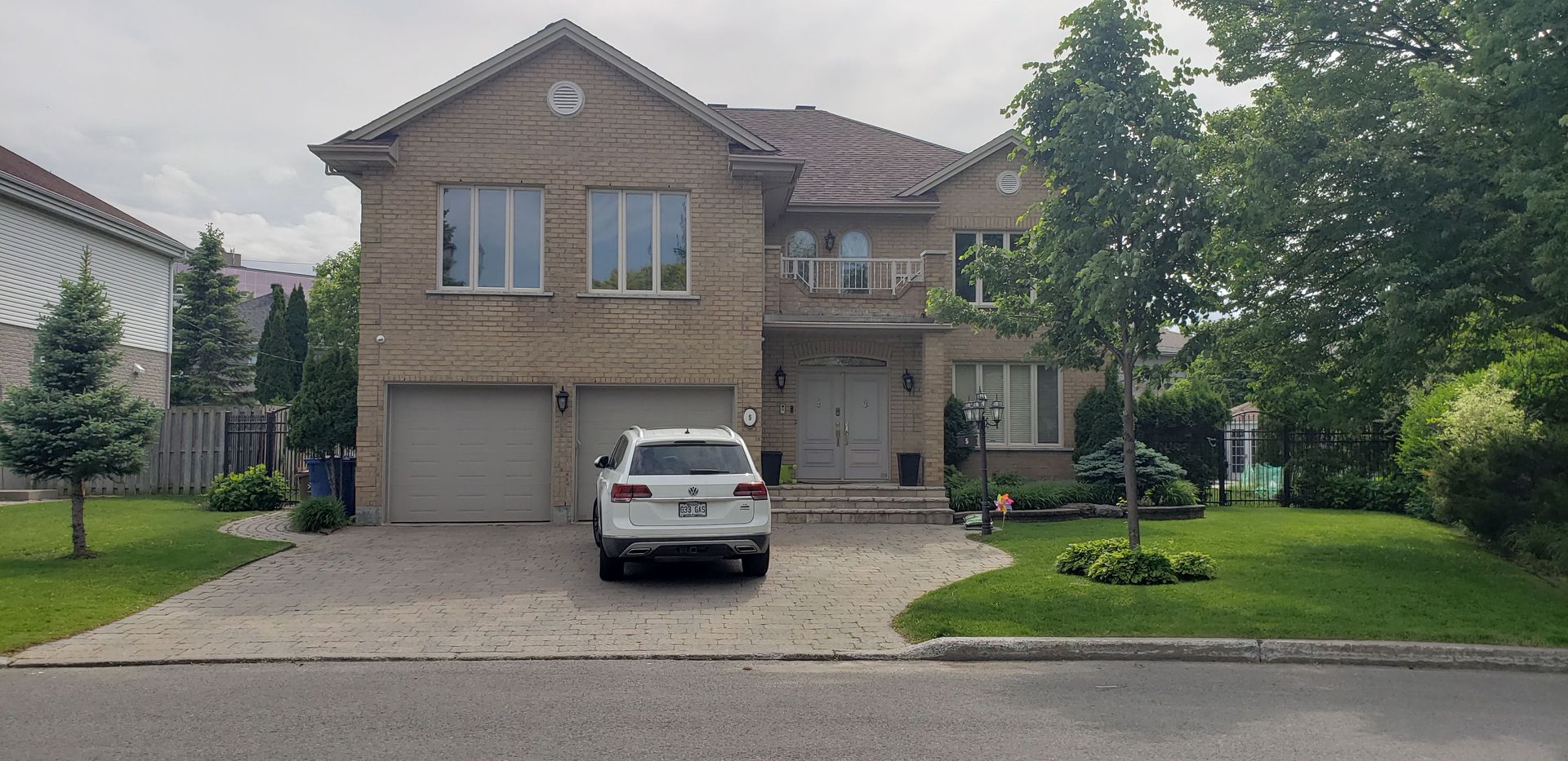 Une voiture blanche est garée devant une grande maison en brique.