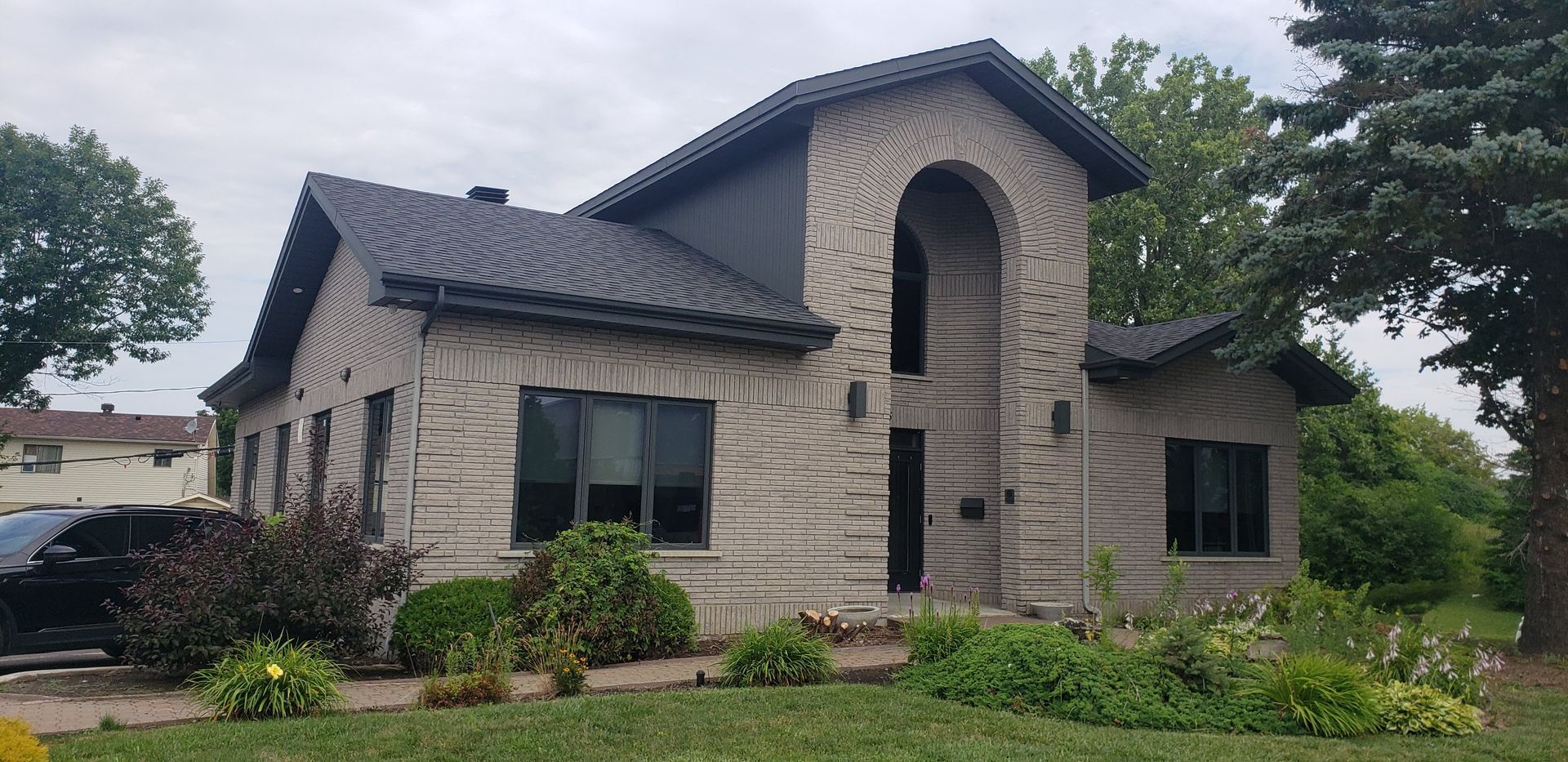 Une grande maison en brique avec un toit noir et une voiture garée devant.