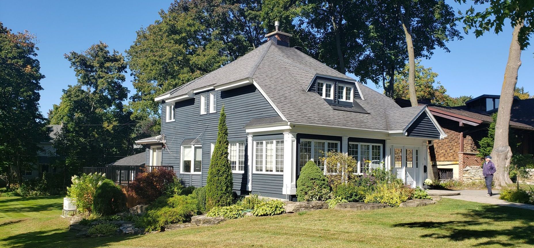 Une grande maison au toit gris est entourée d'arbres par une journée ensoleillée.
