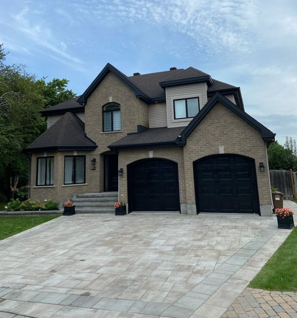 Une grande maison en brique avec deux portes de garage noires