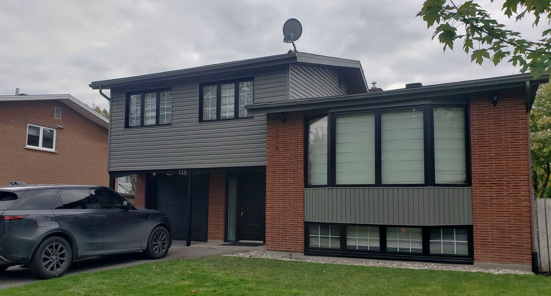 Une voiture noire est garée devant une maison en brique.