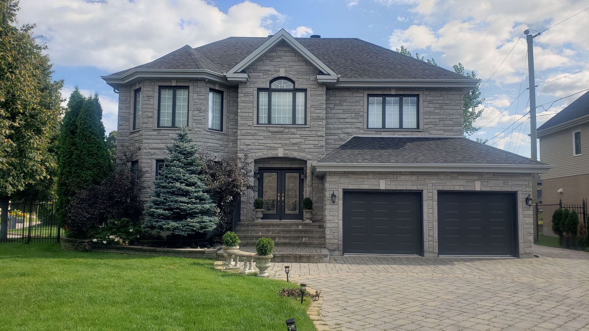 Une grande maison en brique avec deux garages est située au sommet d'une pelouse verdoyante.