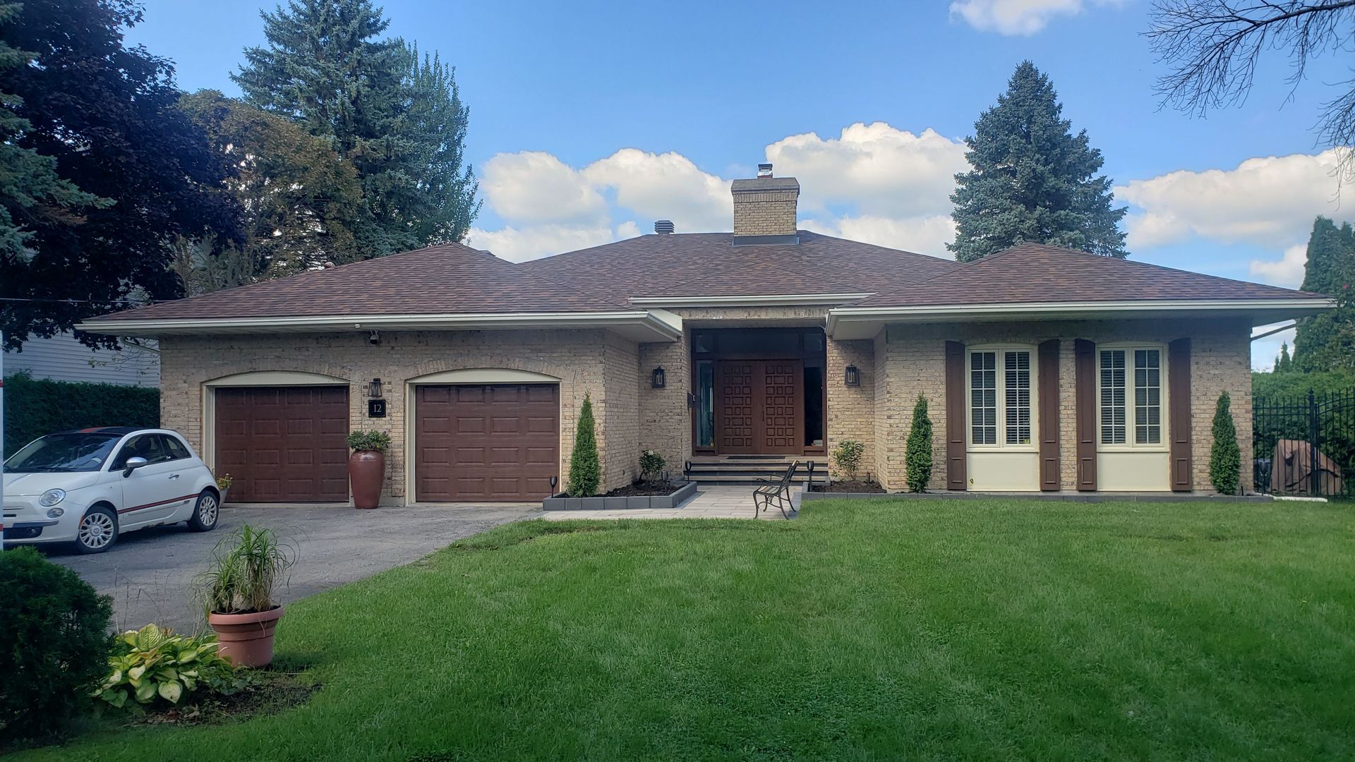 Une voiture blanche est garée devant une maison en brique