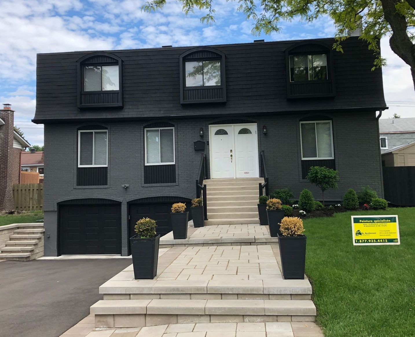 Une maison noire avec un panneau jaune devant