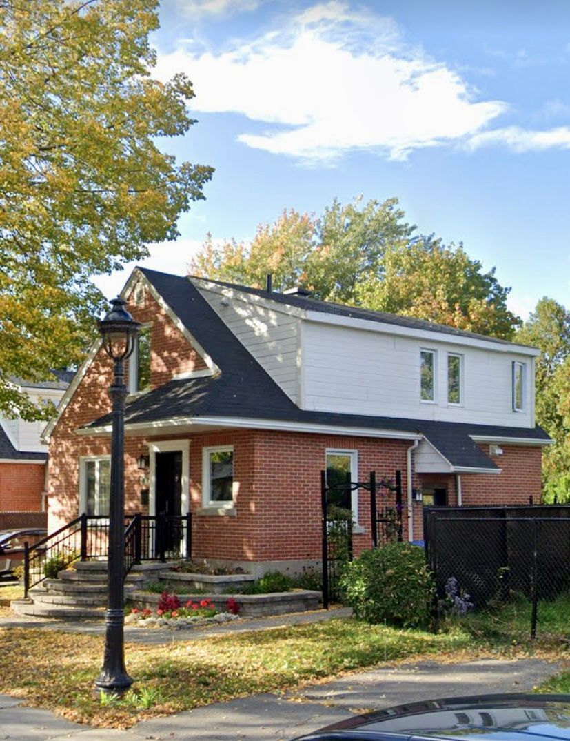 Une maison en brique avec un toit noir et une voiture garée devant