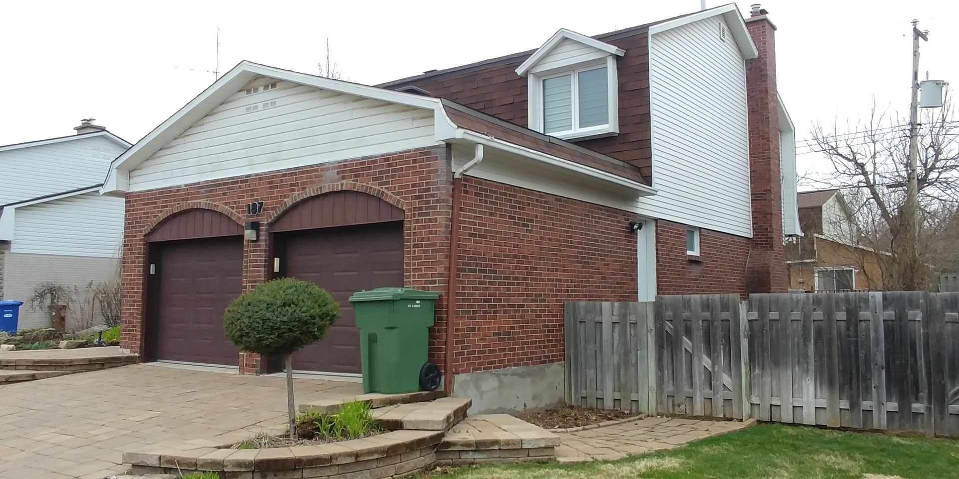 Une maison en brique avec une poubelle verte devant