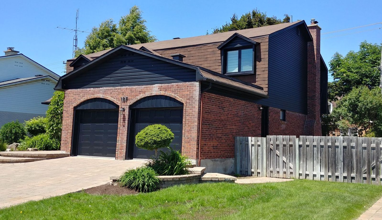 Une maison en brique avec des portes de garage noires et une clôture blanche