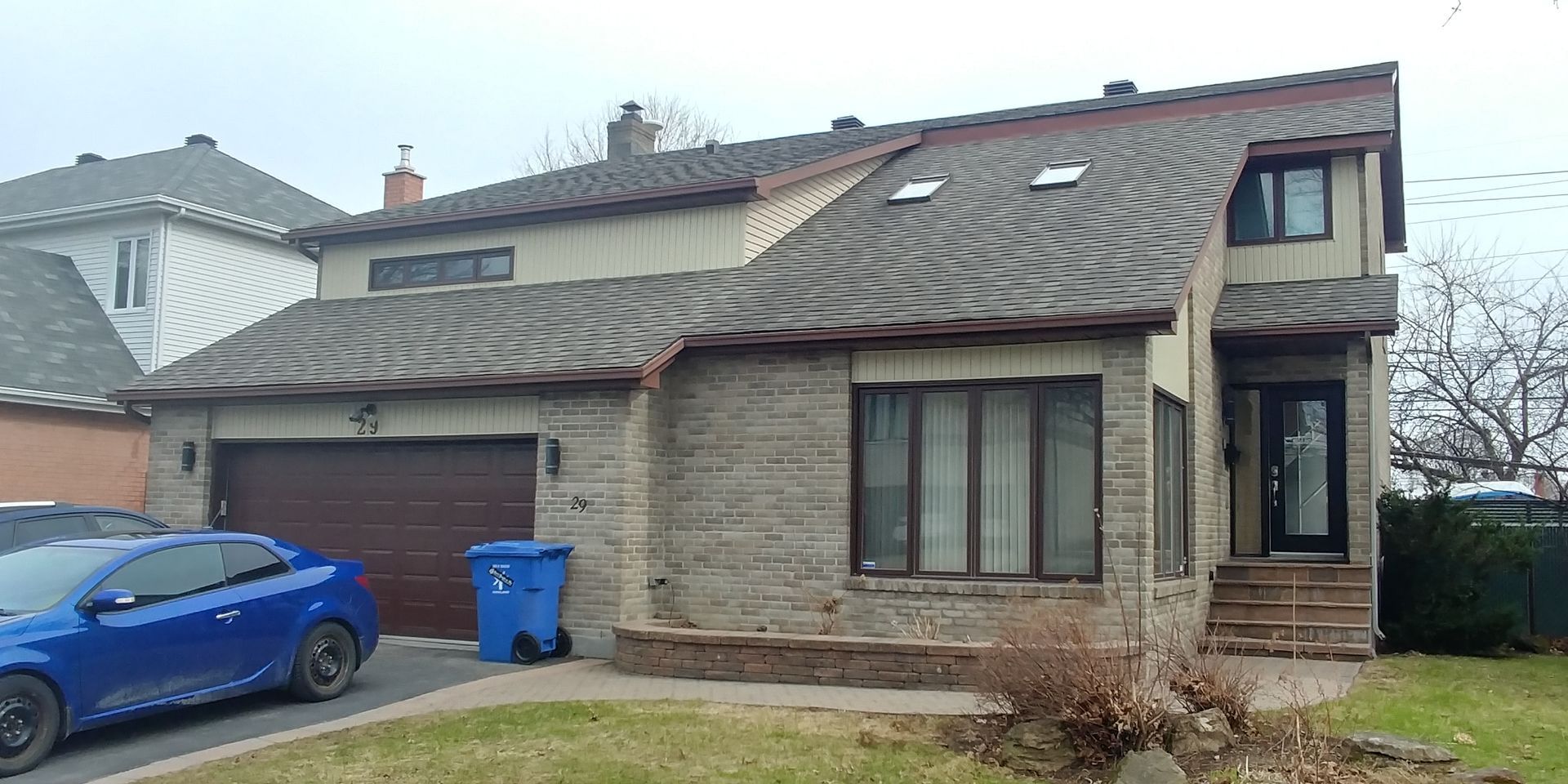 Une voiture bleue est garée devant une maison en brique.