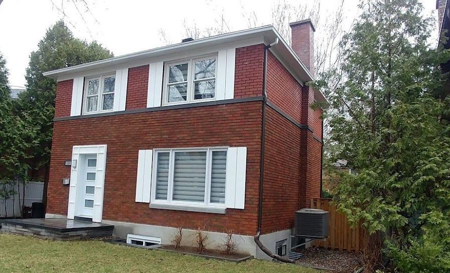 Une maison en brique rouge avec des volets blancs aux fenêtres