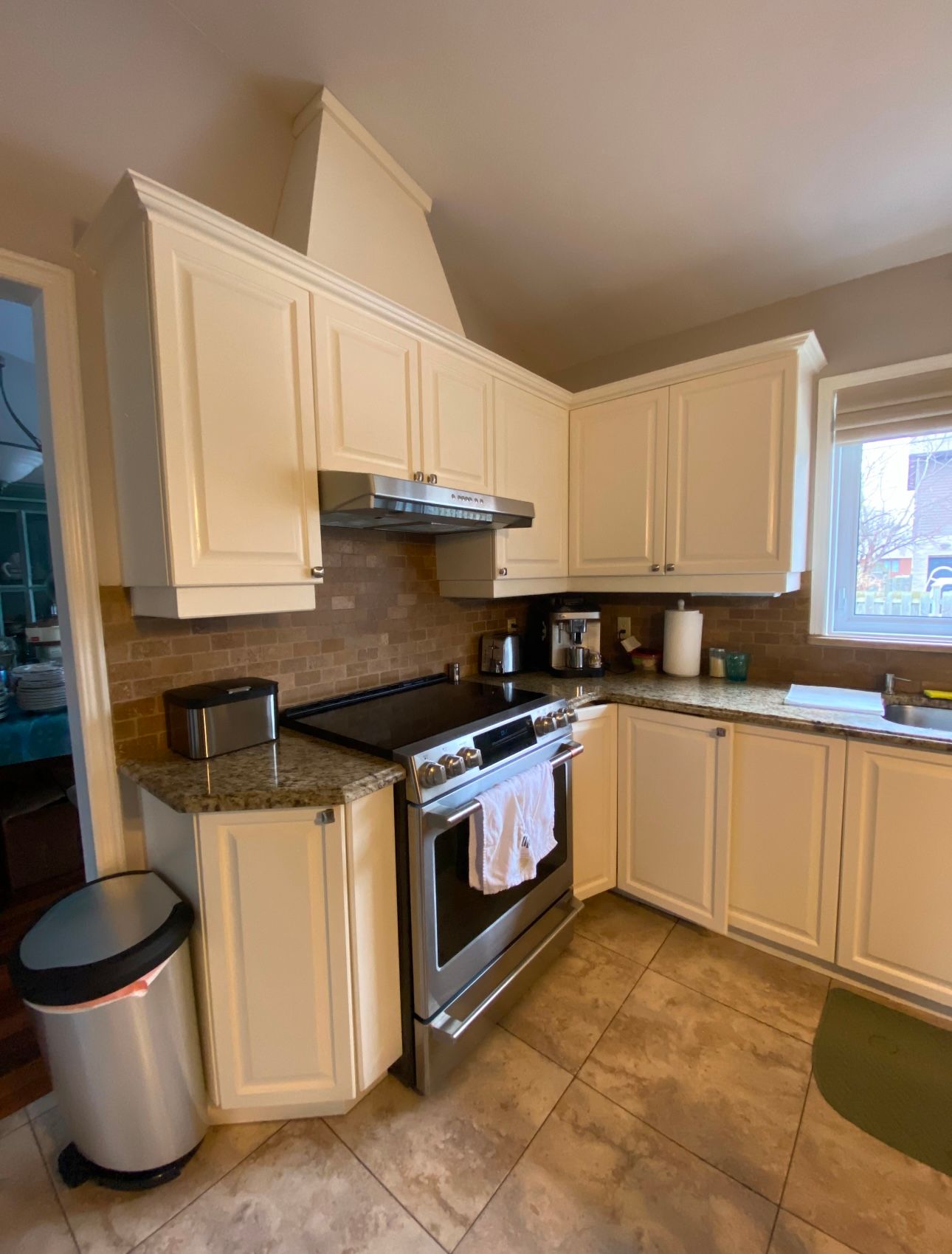 Une cuisine avec des armoires blanches, une cuisinière, un évier et une poubelle.