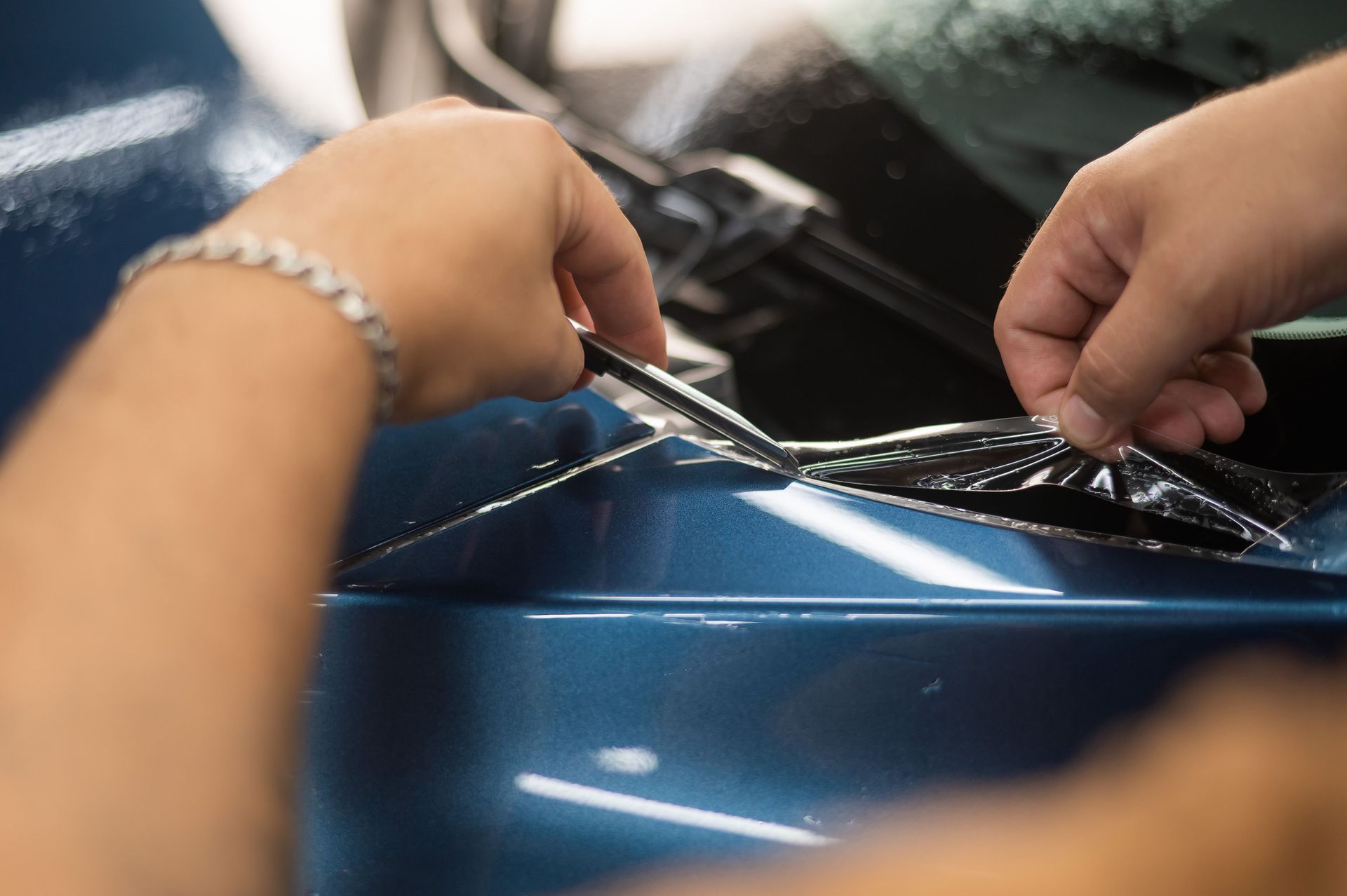 A person is wrapping a blue car with plastic wrap.