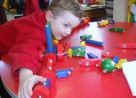 Litltle boy playing with coloured shapes on a red table