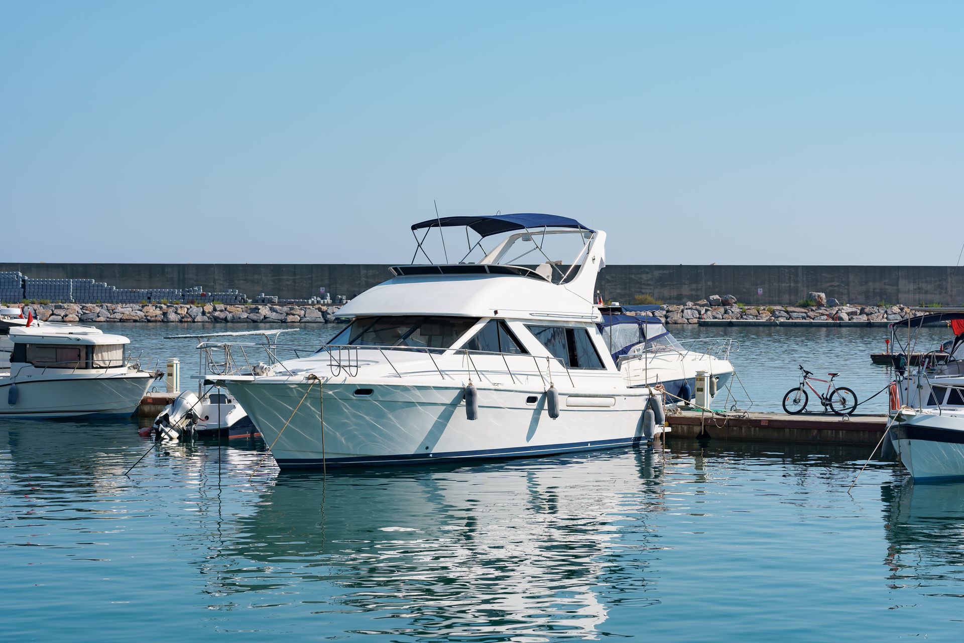 White yacht docked in calm harbor water beside smaller boats under a clear blue sky