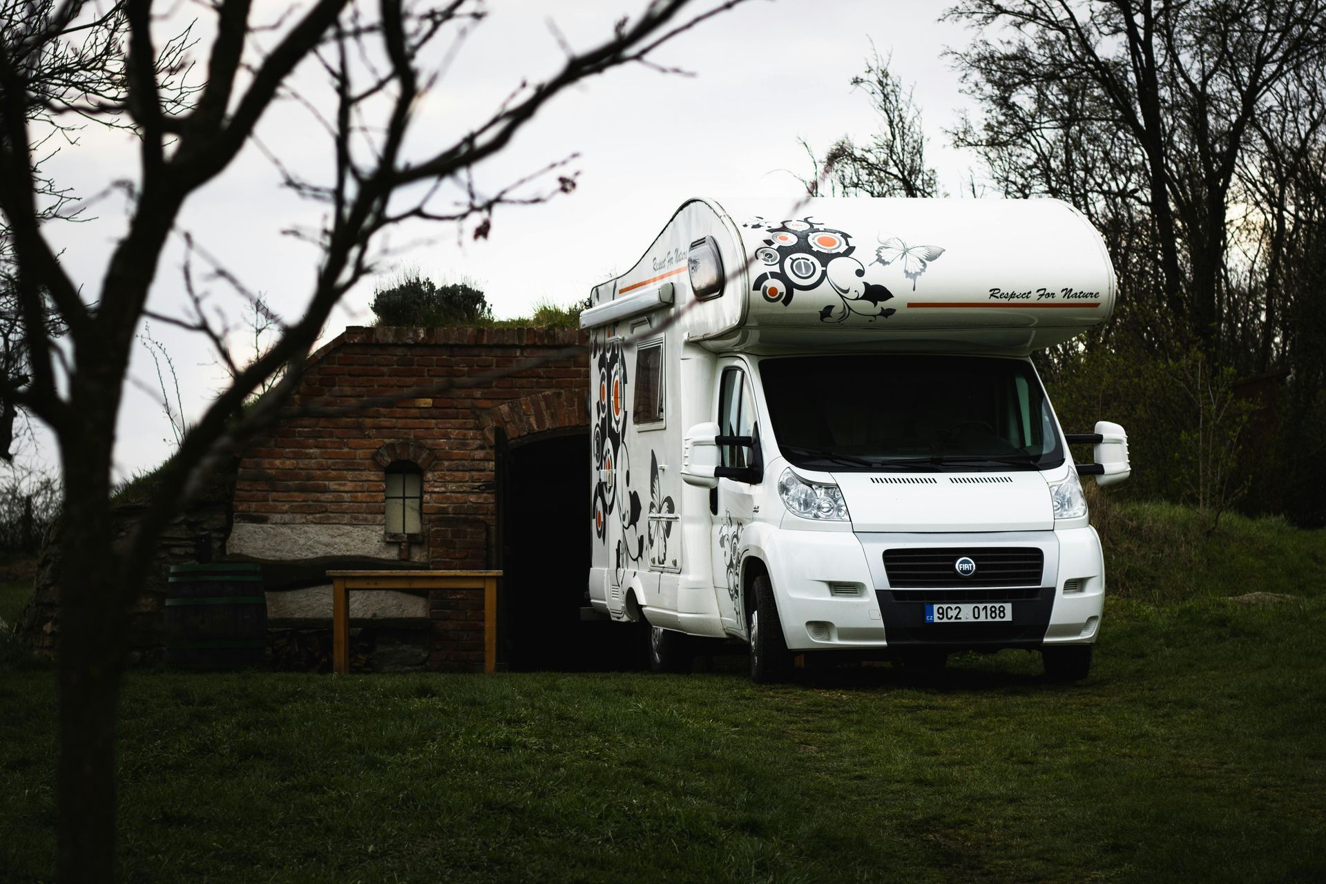 White camper van parked on grass beside a brick building under bare trees
