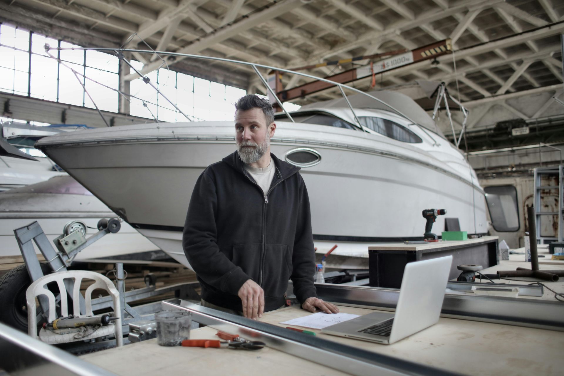 Man standing beside a laptop in a boatyard, with a large white yacht in the background.