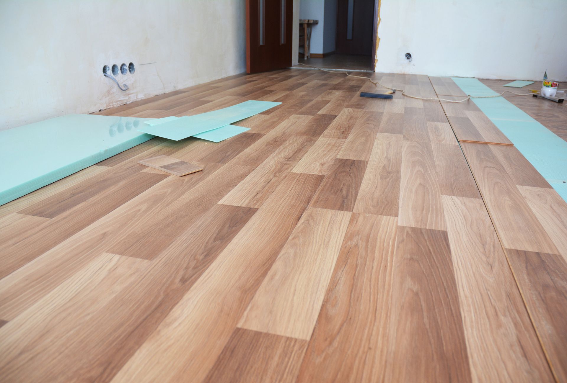 Wooden laminate flooring installation in progress; floorboards laid, with underlayment visible.