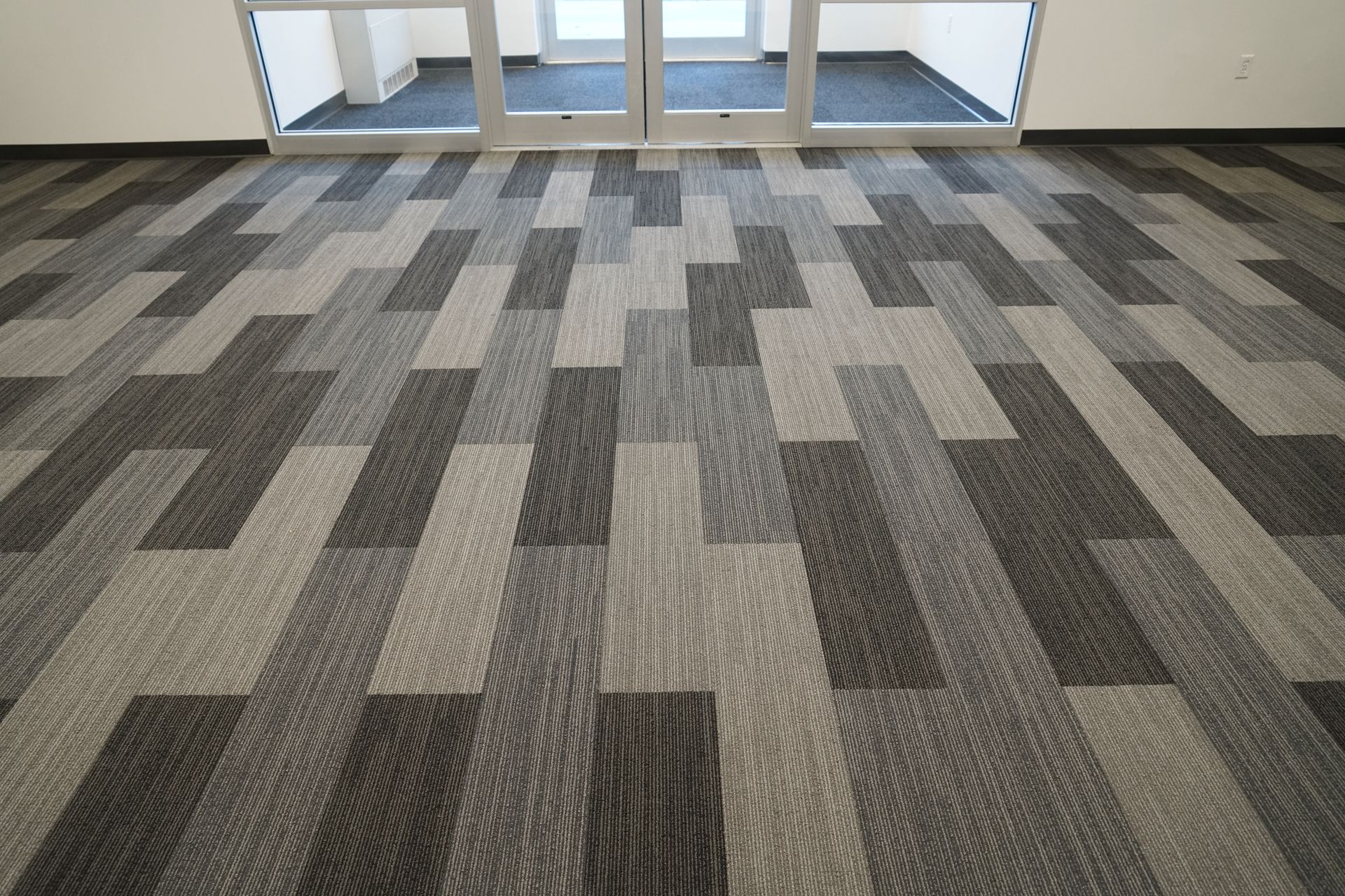 Carpeted floor with a geometric pattern of gray rectangles near glass doors.