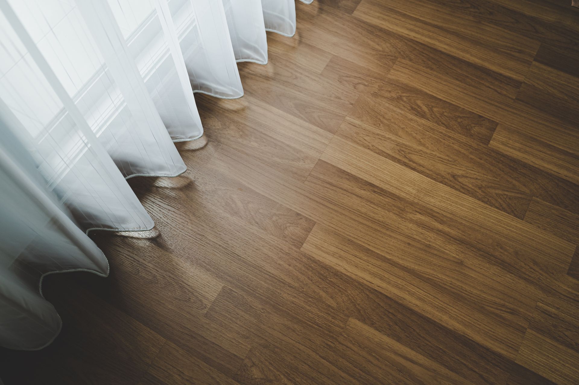 Hardwood floor with white sheer curtains. Sunlight streams through.