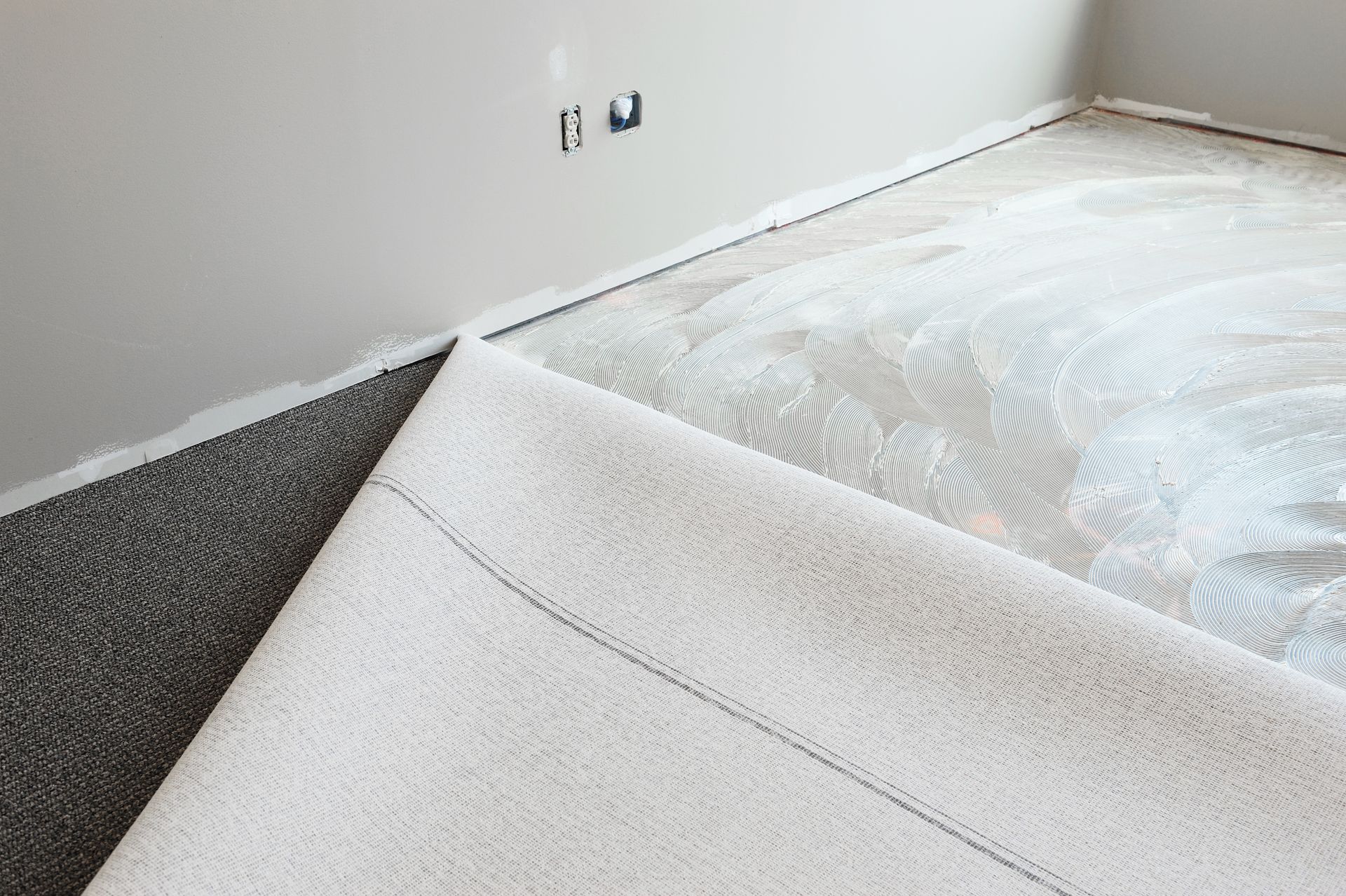 Carpet being installed in a room. White carpet rolled back, exposing the subfloor and black adhesive.