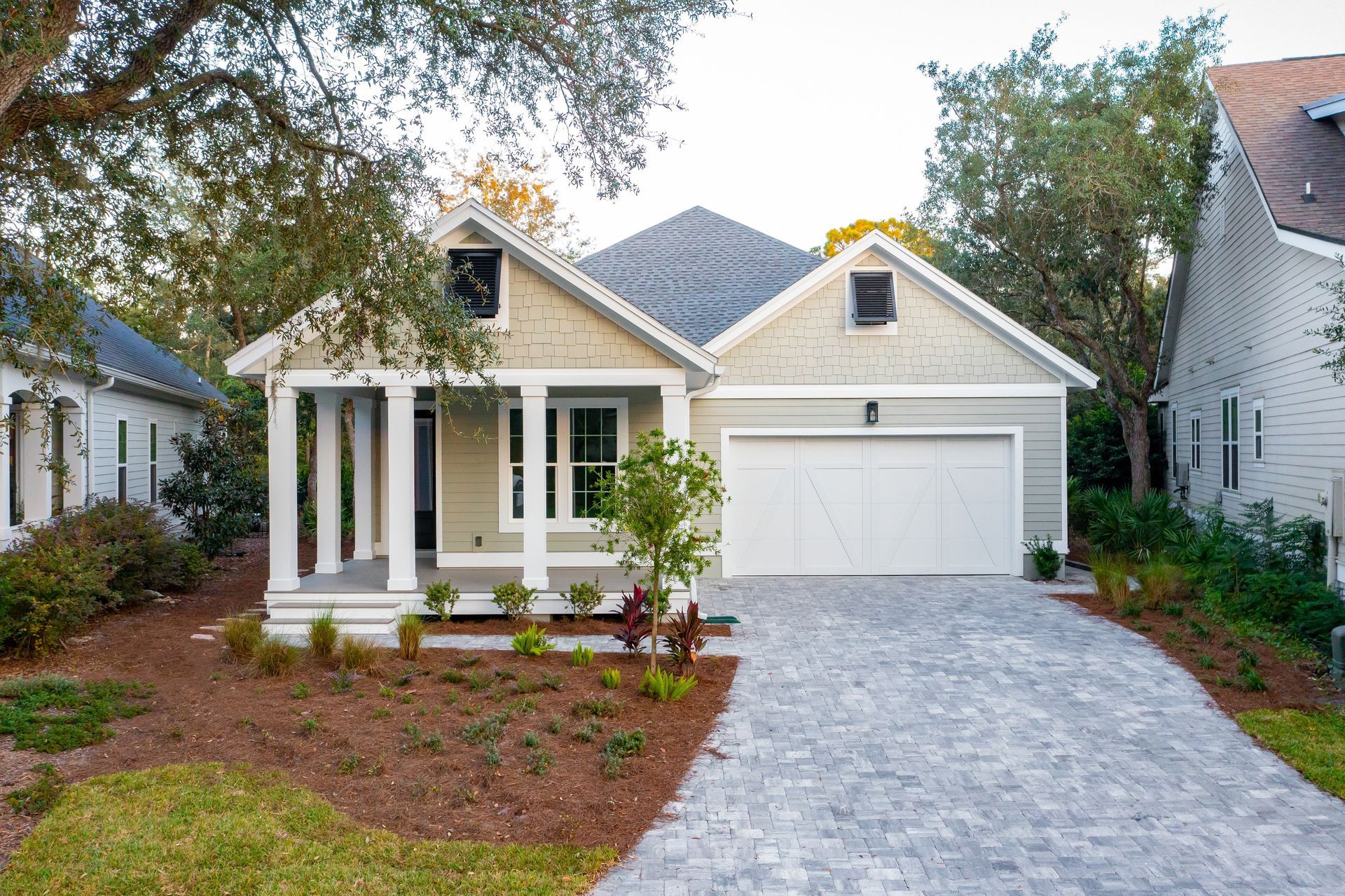 Single-story white house with gray roof, front porch, garage, and stone driveway surrounded by landscaping