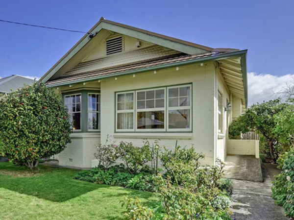 Tan bungalow house with green trim, lawn, and walkway.