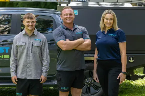 Three people in work attire stand in front of a truck. One has arms crossed. All are smiling.