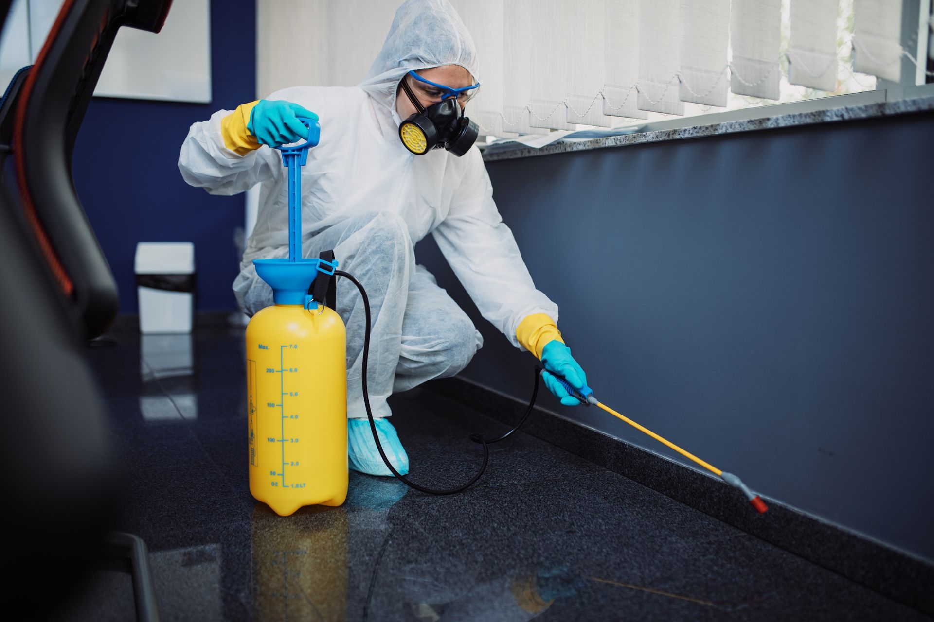An exterminator in workwear is spraying pesticide with a sprayer