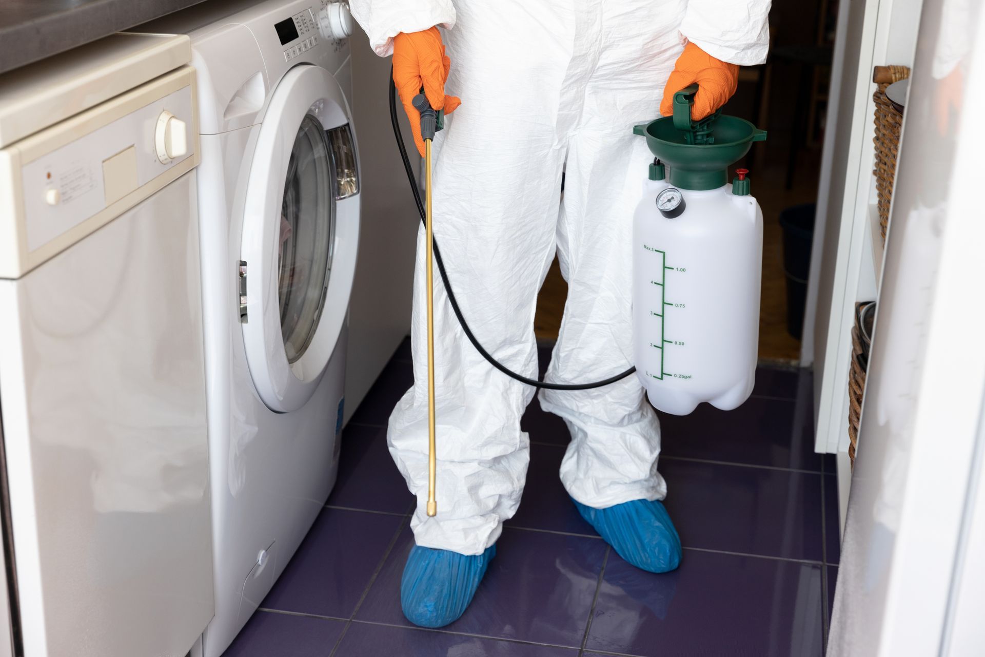 A partial view of an exterminator in a suit providing pest control services in a laundry area.