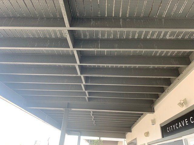 Gray wooden ceiling of a building's covered exterior. Support beams visible, lit by natural light.