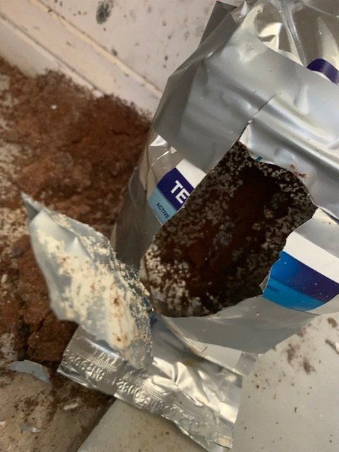 A torn silver bag with dark brown powder spilling out onto a surface.