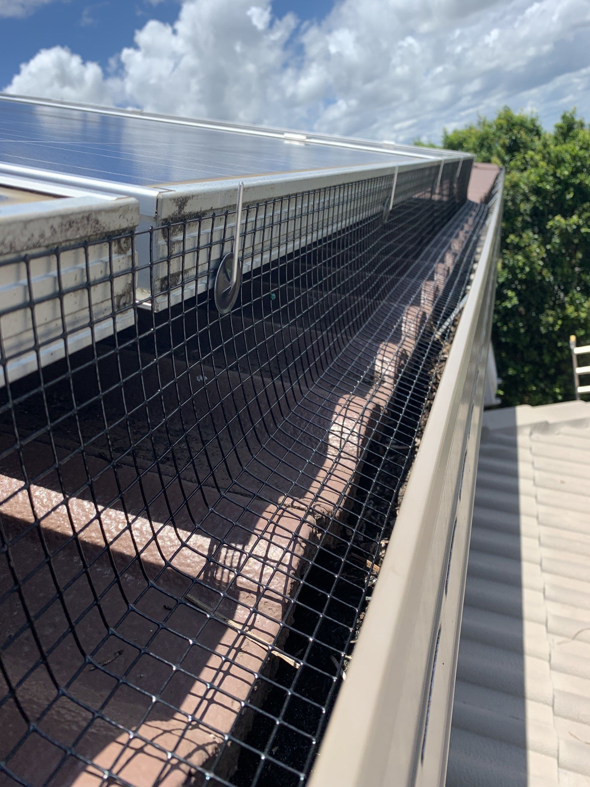 Black mesh gutter guard installed on a tiled roof, near solar panels.