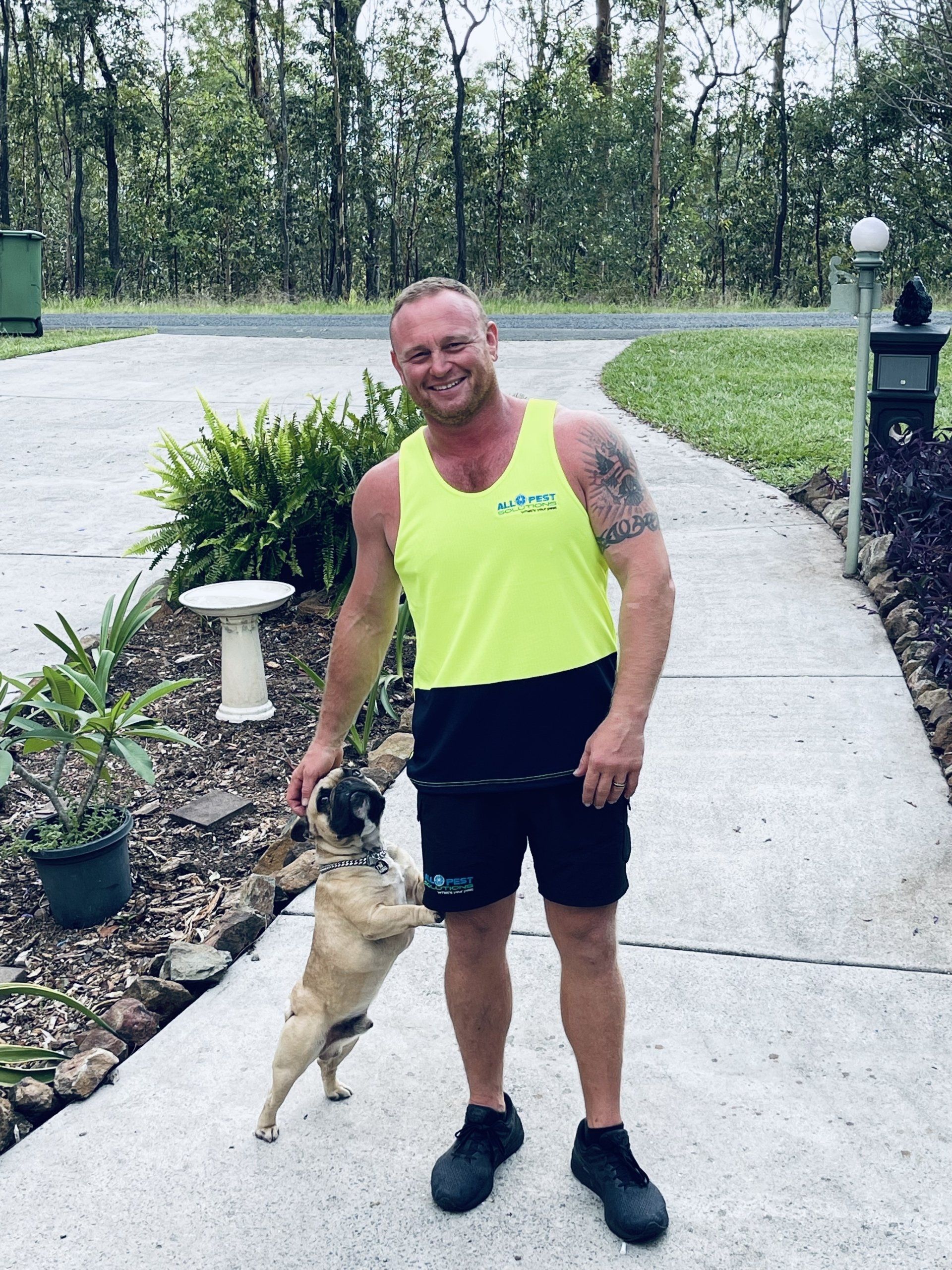 Man in neon top and black shorts smiles with dog on paved path.