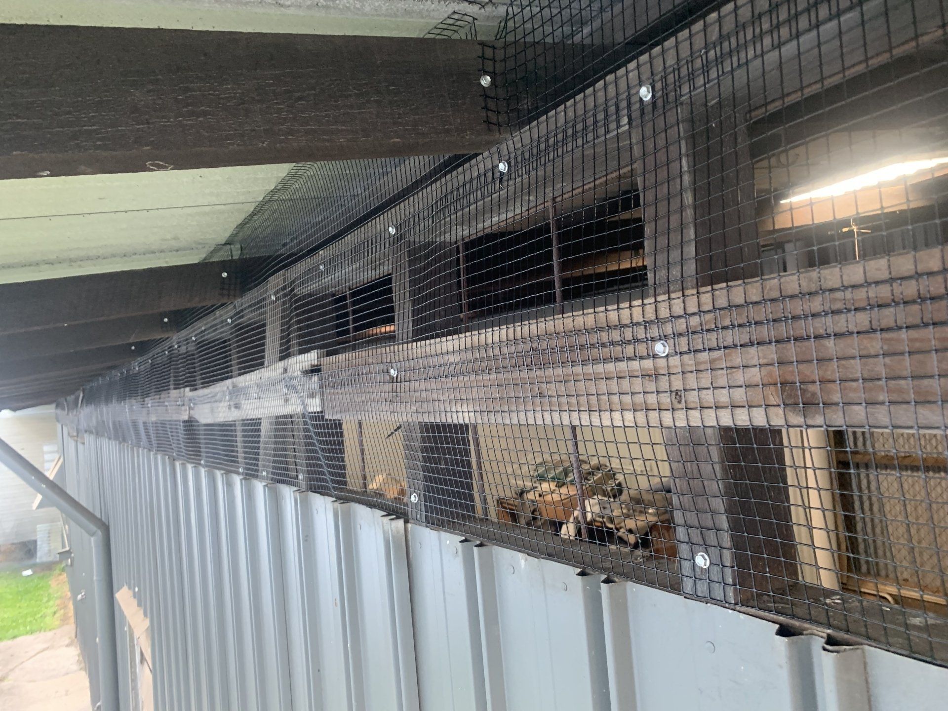 Black mesh netting covers a wooden structure attached to a gray metal building, protecting the open spaces.