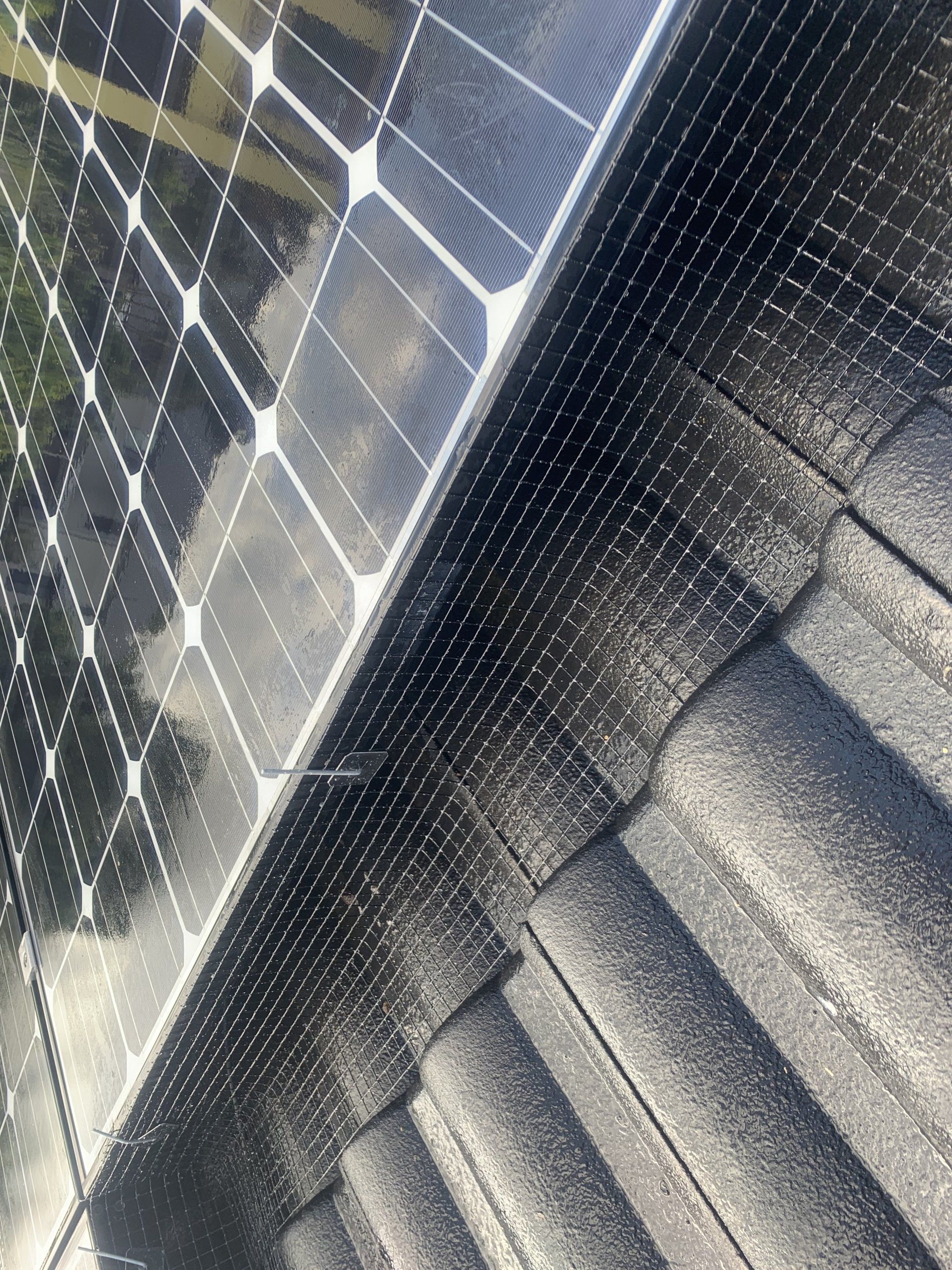 Solar panel installed on a black tiled roof with a mesh covering.