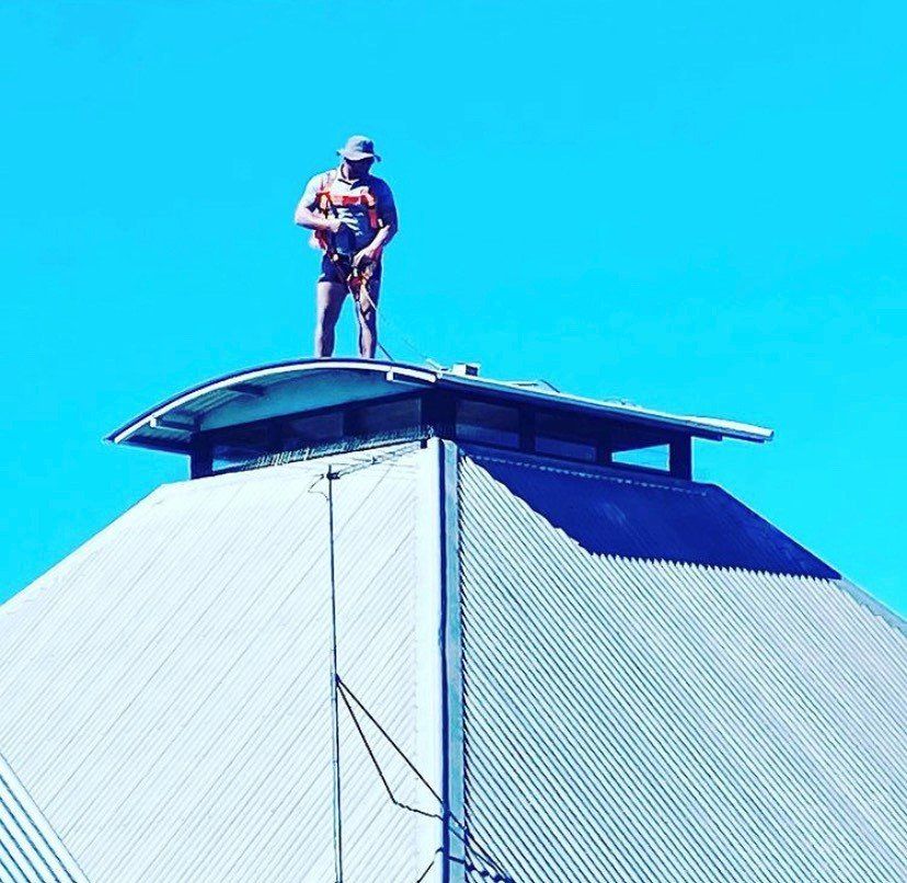 Person on a roof wearing a hat and harness. Clear blue sky.