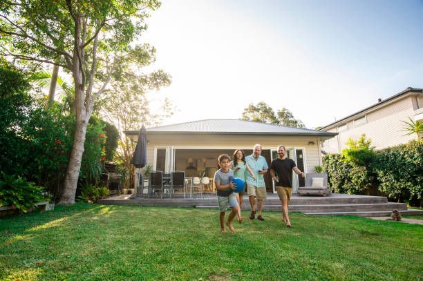 Family playing in backyard, near a house with open back doors. Sunlit day.