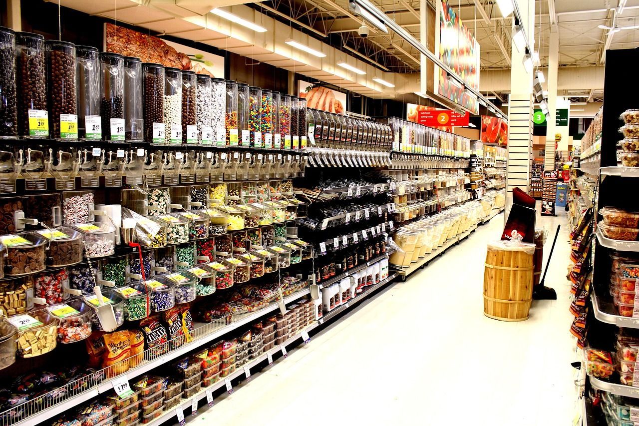 Grocery store aisle with bulk food dispensers and packaged goods on shelves.