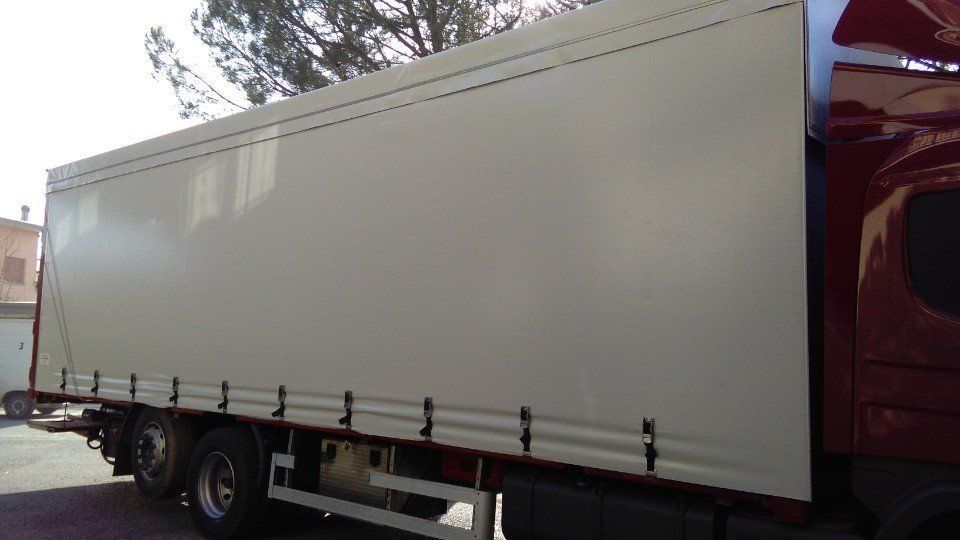 Un camion rosso con un telo bianco sul retro è parcheggiato in un parcheggio.