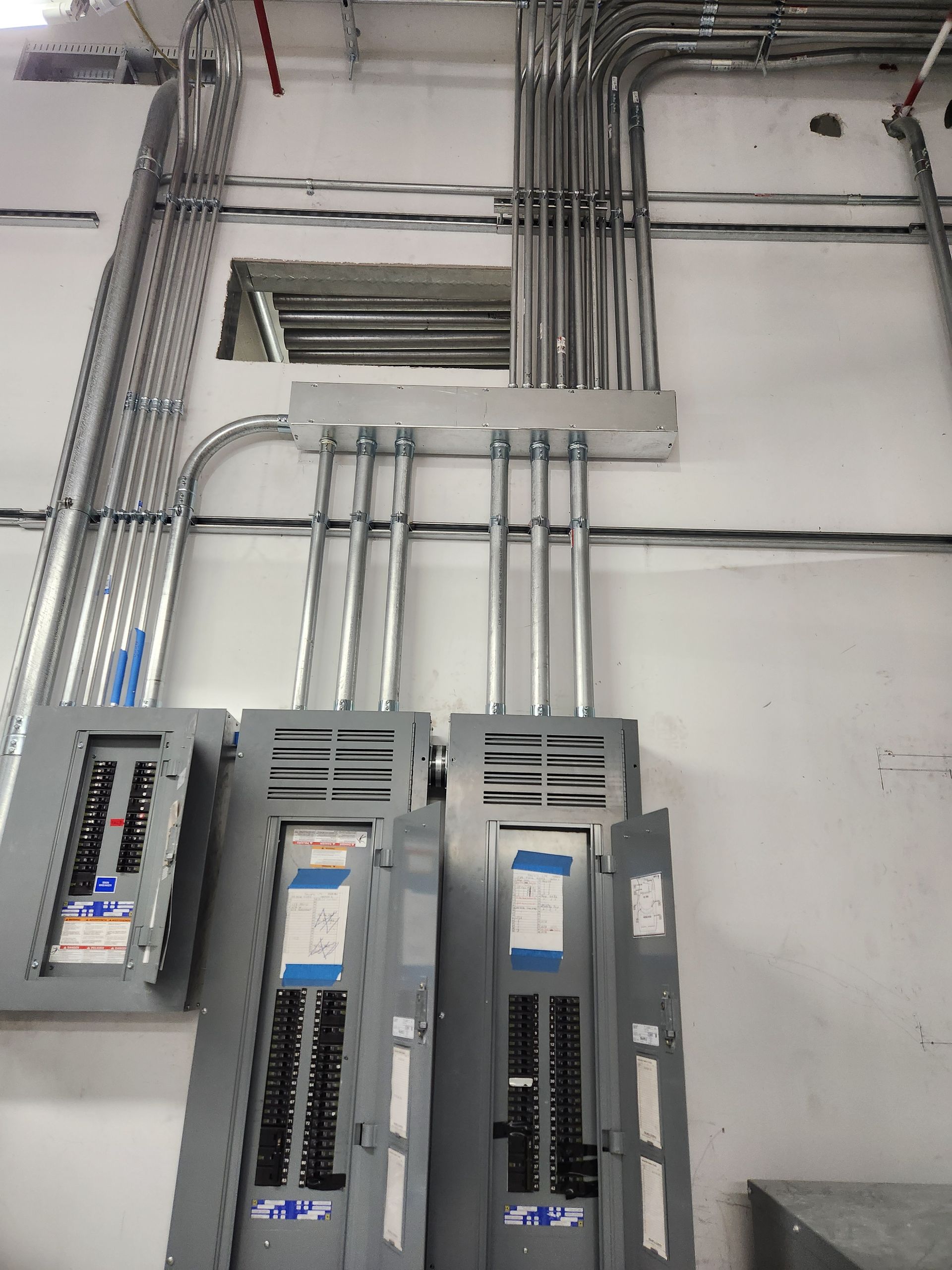 Electrical breaker panels and conduit pipes mounted on a wall in an industrial utility room