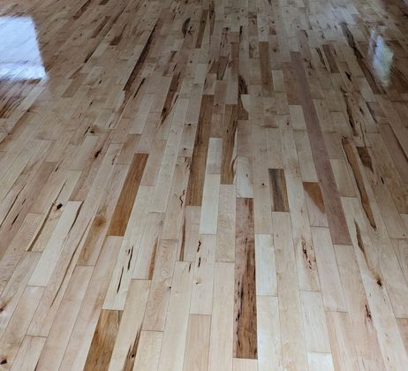 Polished hardwood floor with light beige, tan, and dark brown wood grain variations in a linear plank pattern.
