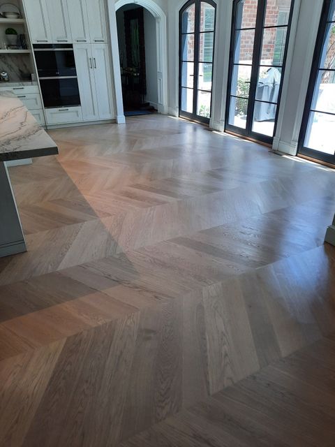 Light-toned wooden flooring laid in a decorative chevron pattern inside a modern kitchen with French doors.