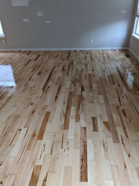 Polished hardwood floor with light beige, tan, and dark brown wood grain variations in a linear plank pattern.