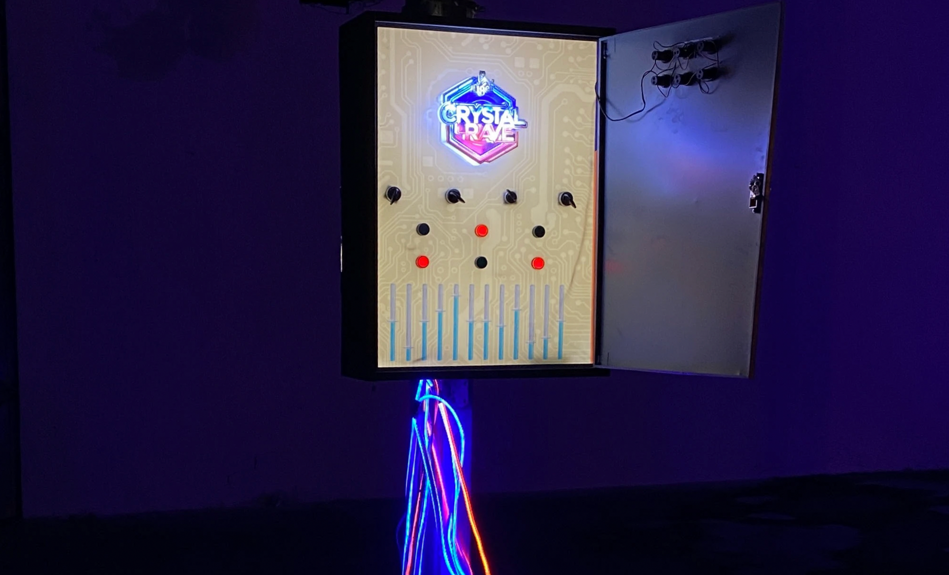 Illuminated interactive game with buttons and a logo, mounted on a light-up stand, in a dimly lit space.