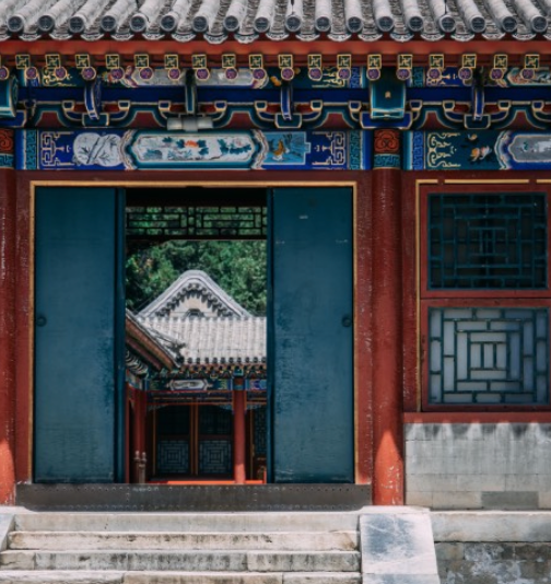 Ornate red and blue Chinese building, open doorway framing another similar structure in the distance.