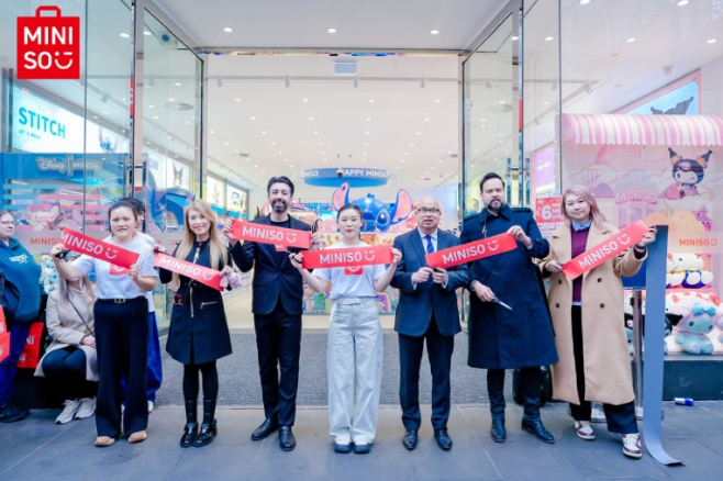 People cutting a ribbon at a MINISO store opening, holding red MINISO signs.