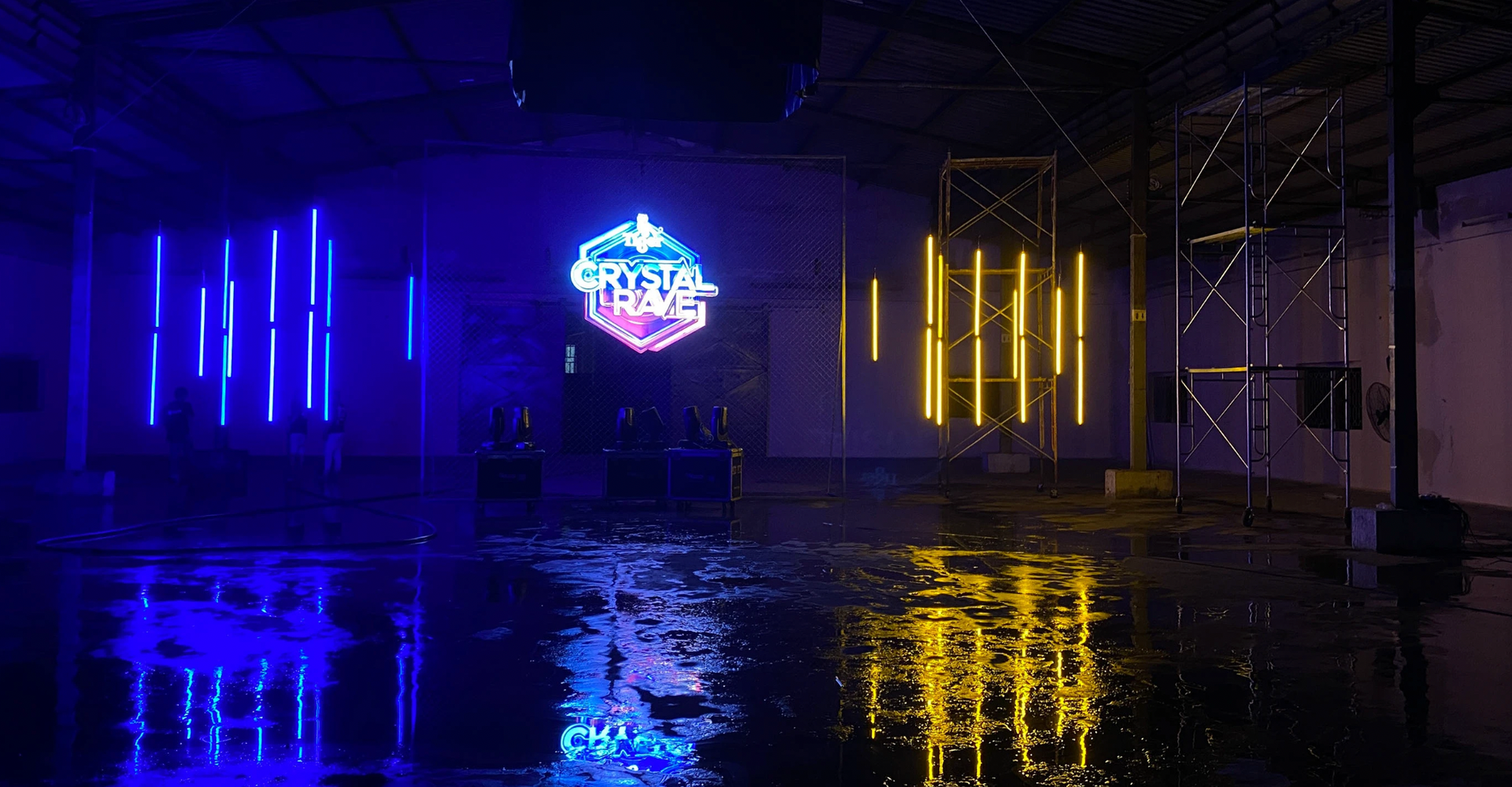 Neon light installation in warehouse, featuring blue, yellow, and pink lights reflecting in a wet floor.