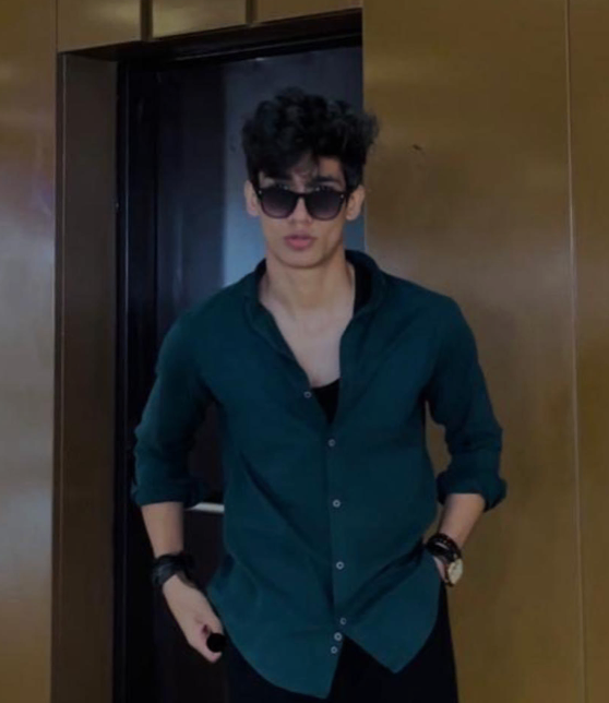 Woman smiles with eyes closed, hand in hair, wearing polka dot dress, wood background.