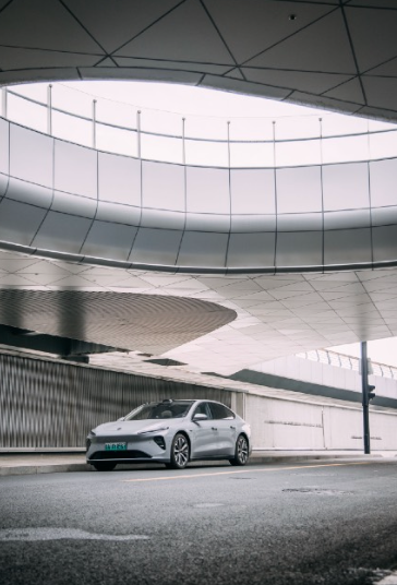 Silver electric vehicle under a modern, curved, architectural structure with glass and concrete.