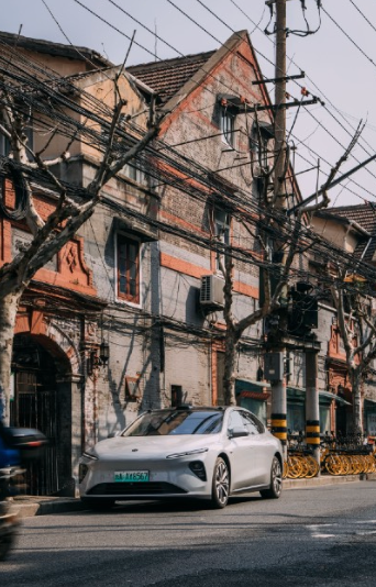 White electric car parked on a street in front of an aged brick building with power lines overhead.