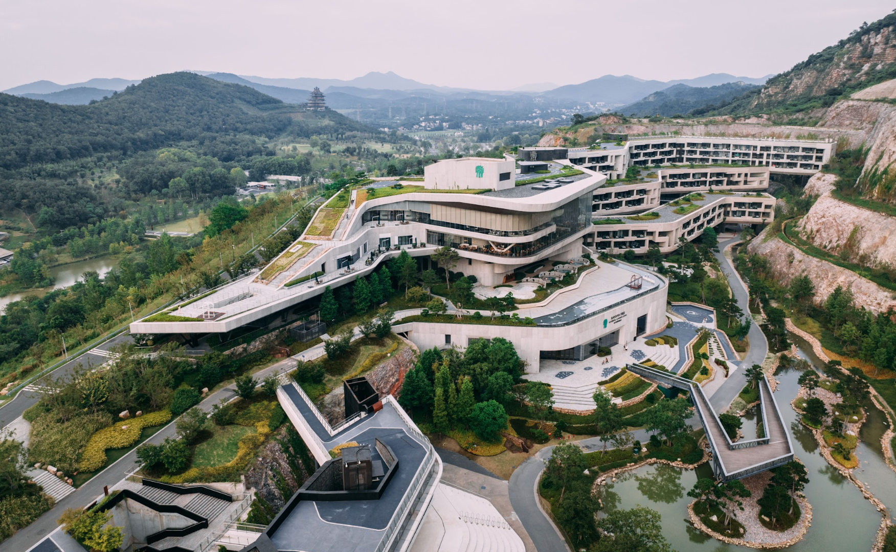 Modern, multi-level building integrated into a hillside landscape. White and beige with green landscaping.